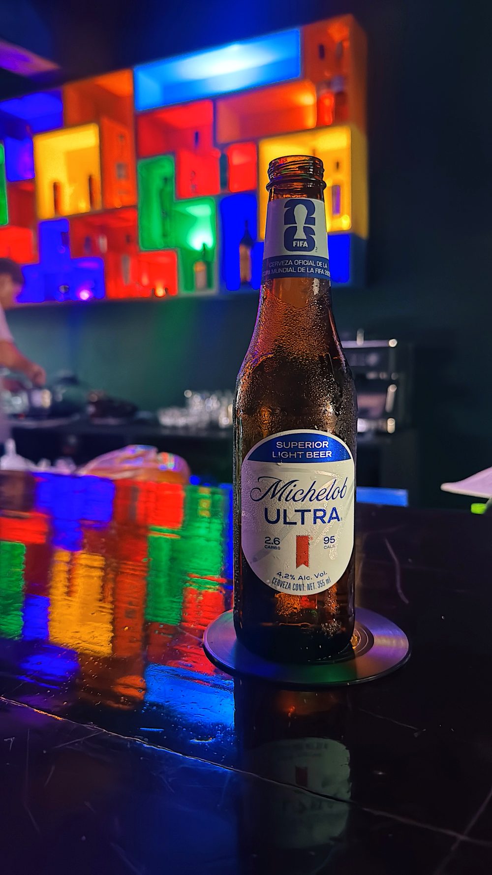 Cerveza servida sobre la barra negra, con la pared de bloques reflejándose en la superficie